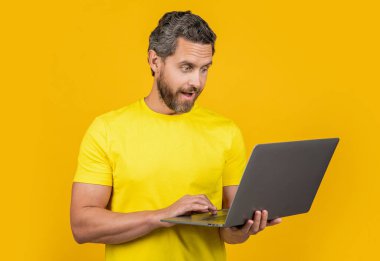 Şaşırmış adam blogcusu sarıda izole edilmiş. Arka planda bir blog yazarı. Stüdyoda blog yazarı. Dizüstü bilgisayarı olan bir adam blogcusunun fotoğrafı.
