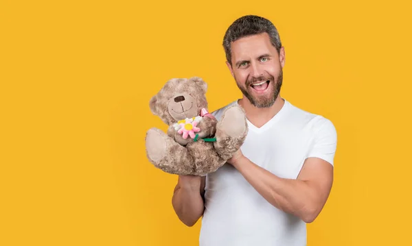 stock image photo of positive guy holding valentine toy bear. guy hold valentine toy bear isolated on yellow background. guy hold valentine toy bear in studio. guy with toy bear for valentine day.