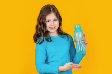 Sarı arka planda spor şişesi sunan çocuk.