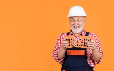 Sarı arka planda kasklı yaşlı adam gülümsüyor..