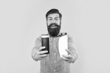 happy brutal bearded man offer shampoo bottle on yellow background, haircare.