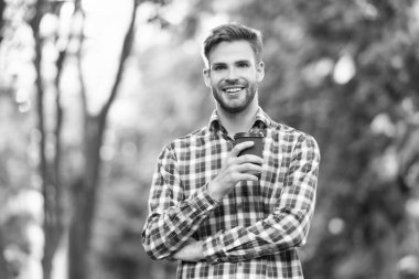 Kahve fincanıyla kareli gömlekli genç adam gülümsüyor..