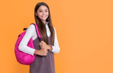 Sarı arka planda okul çantasıyla çocuk gülümsemesi.