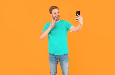 Cep telefonlu video blogcusu barış jesti gösteriyor. Akıllı telefondan video blogu yapan adam. Telefonla blog yazıyorum. Etkileyici ya da danışman. Mutlu adam selfie çekiyor. erkek blogcu.