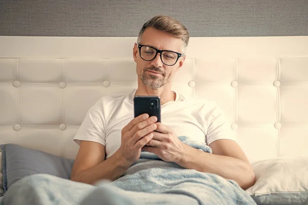 Cheerful Mature Man Bed Chatting Phone Wearing Eyeglasses —  Fotos de Stock