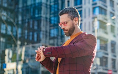 Dakik adamın fotoğrafı. Elle kontrol zamanı. Dışarıda ceketli dakik bir adam var. Dakik adam caddede zamanı kontrol ediyor. Dakik adam dışarıda zamanı kontrol et.