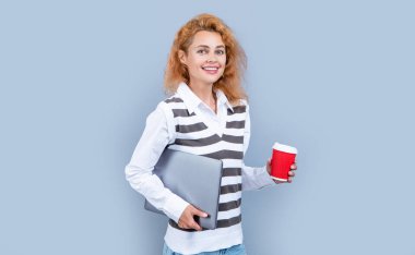 Dizüstü bilgisayarı ve kahvesi olan serbest çalışan neşeli bir kadın. Bilgisayarı tutan serbest çalışan bir kadın. Gri arka planda kahvesi olan serbest çalışan bir kadın. Stüdyoda serbest çalışan kadın..