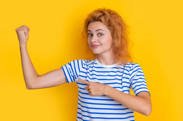 redhead woman show biceps isolated on yellow background. portrait of young redhead woman in studio. adult redhead woman portrait.
