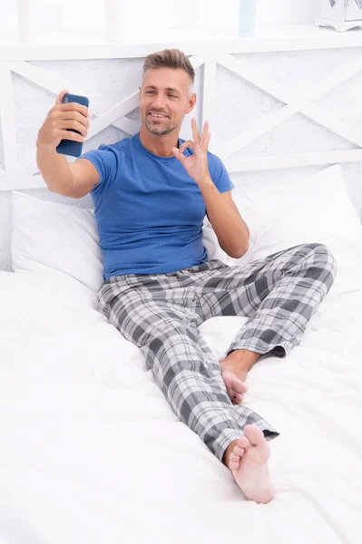 blogging man with phone wear pajama, ok. blogging man with phone in bed. photo of blogging man with phone at home. blogging man with phone in bedroom.