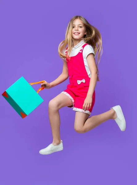 positive teen girl jumping after shopping on background. photo of teen girl jumping after shopping. teen girl jumping after shopping isolated on purple. teen girl jumping after shopping in studio.