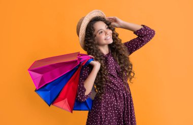 cheerful child with curly hair hold shopping bags on yellow background.