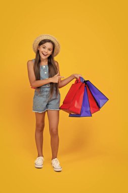 happy teen girl pointing finger on shopping bags on yellow background. full length.
