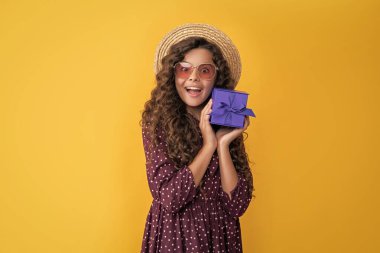 happy girl with curly hair hold present box on yellow background.