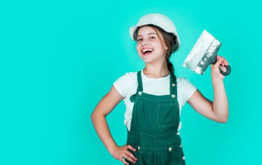 Ev tadilatı. Aletli çocuk. Spatulalı mutlu küçük inşaatçı kız. Genç kız macun bıçağı kullanıyor. Tulumlu ve spatulalı miğferli bir müteahhit. Çocuk duvar macunuyla onarıyor. Boşluğu kopyala.