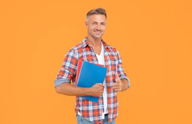 Okul kitaplarını sarı arka planda tutan gündelik parmakla işaret eden mutlu çocuk, öğrenci..