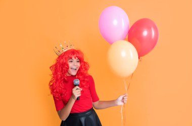 Sarı arka planda mikrofonlu ve parti balonlu mutlu çocuk..