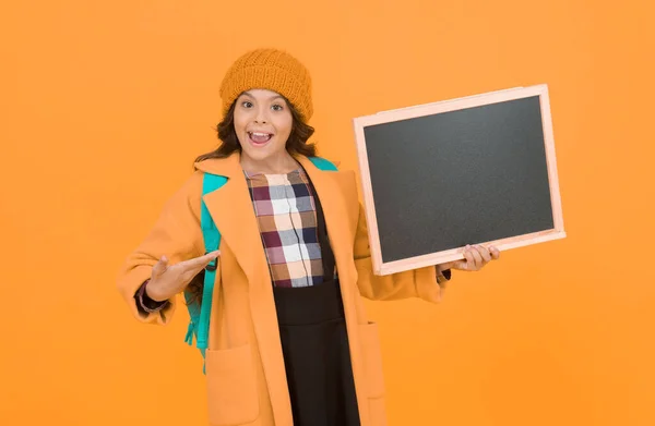 幸せな女の子の黒板黄色の背景にポイントします 黒板のない小さな子供 小さな子供は学校の黒板を持っています 広告のBlackboard スペースのコピー — ストック写真