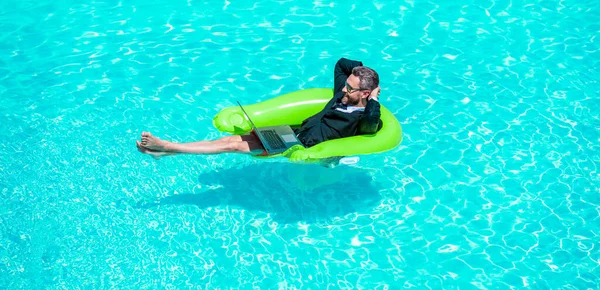 relaxing business manager work in summer with laptop. photo of business manager wearing suit work in summer pool. business manager work in summer. business manager work in summer at swimming pool.