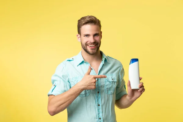 man hold shampoo cosmetics isolated on yellow, point finger. man hold shampoo cosmetics in studio background. photo of man hold shampoo cosmetics. man hold shampoo cosmetics.