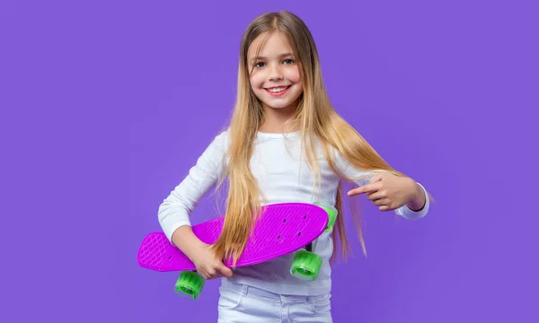 紫色で隔絶されたスケートボーダーで指を指している少女 スタジオの10代の少女スケートボーダー 背景に10代の少女スケートボーダー 10代の少女スケートボーダーの写真 — ストック写真