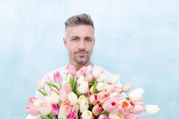 stock image photo of smiling man with valentines day bouquet for holiday. man with valentines day bouquet. man with valentines day bouquet in studio. man with valentines day bouquet isolated on blue background.