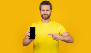 Adam arka planda akıllı telefon uygulaması gösteriyor, işaret ediyor. Stüdyoda akıllı telefon uygulaması gösteriyor. Akıllı telefon uygulaması gösteren bir adamın fotoğrafı. Akıllı telefon uygulaması gösteren adam sarıda izole edildi.