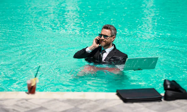 stock image cheerful business manager work in summer. business manager work in summer at swimming pool. business manager work in summer has phone call. photo of business manager wearing suit work in summer pool.