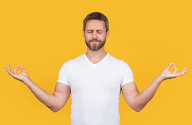 Sakallı adam, sarı gömlekle meditasyon yapıyor. Meditasyon stüdyosunda meditasyon yapan bir adam. Meditasyon yapan adamın beyaz gömlekli fotoğrafı. Adam günlük kıyafetlerle meditasyon yapıyor. meditasyon kavramı.