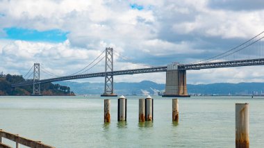San Francisco, ABD 'de deniz suyu üzerinde bulutlu gökyüzü altında köprü yapısı mimarisi.