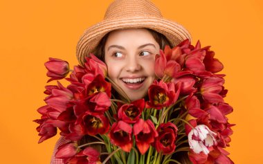 happy kid in hat hold spring tulip flowers on yellow background.