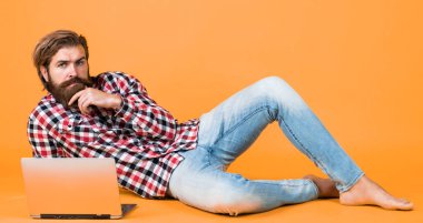 Kaba sakallı, kareli gömlek giyen, sakallı ve bıyıklı bir adam laptopta, işte çalışıyor..