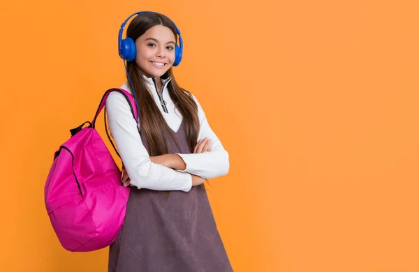 黄色の背景にスクールバックパック付きヘッドフォンで幸せな子供 — ストック写真