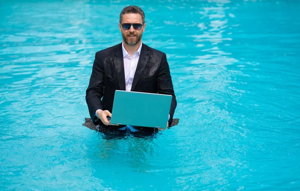 business man working remote with laptop, copy space. photo of business man working remote in summer pool. business man working remote online. business man working remote in swimming pool.