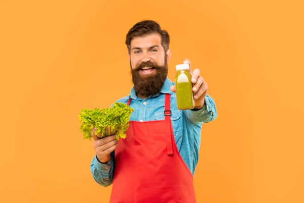 stock image Happy man giving juice bottle holding fresh lettuce yellow background, juice shopkeeper.