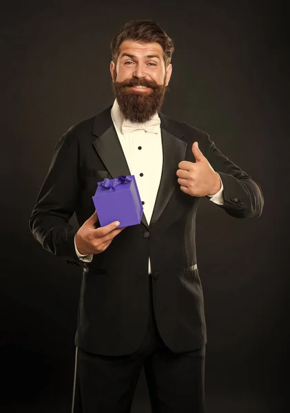 happy man in tuxedo bow tie formalwear on black background with box. birthday. thumb up.