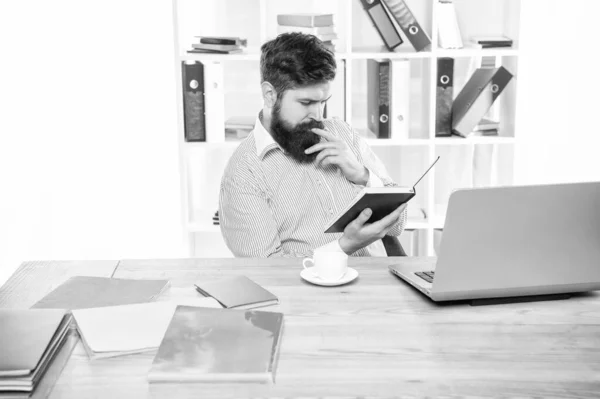 stock image Serious manager reading book sitting at office desk.