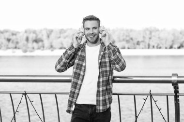 happy handsome man in casual checkered shirt. young unshaven guy listen music in headphones outdoor. male fashion model. education online. listening audio book.