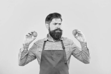 Worried man in red apron looking at fresh limes citrus fruits yellow background, fruiterer.