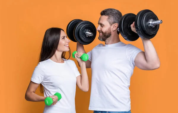 photo of smiling fitness couple with barbell. fitness couple with barbell isolated on yellow background. fitness couple with barbell in studio. fitness couple with barbell in gym.