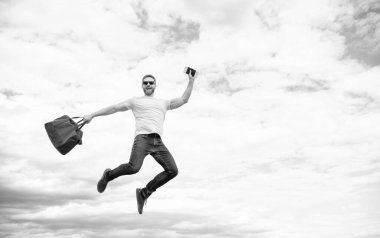 Active guy jumping with travel bag midair sky background, copy space.