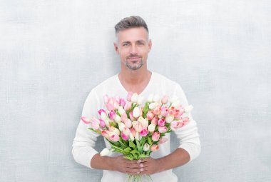 cheerful man with valentines tulips. man with valentines tulips in studio. man with valentines tulips isolated on blue background. photo of man with valentines tulips.