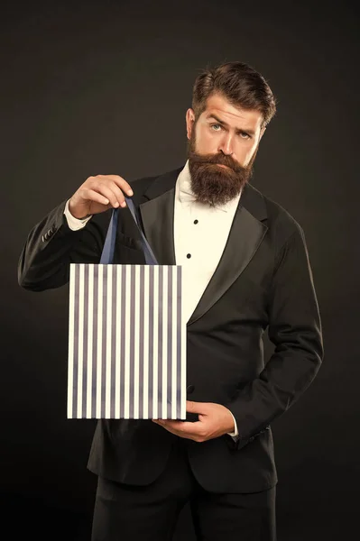 man in tuxedo bow tie formalwear on black background presenting shopping bag. valentines day. copy space.