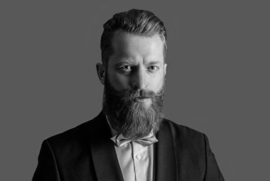 Smokin giymiş bir adamın stüdyosunun yüzü. Zarif smokin giyen bir adam. Smokin modası. Smokinli yakışıklı sakallı adam gri arka planda izole edilmiş..