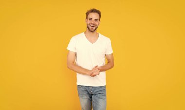 Sarı arka planda sakallı mutlu genç bir adam. Saç ve sakal bakımı. Kendine güvenen ve yakışıklı, tıraşsız adam. Erkek modası. Erkek güzelliği. Beyaz gömlekli kıllı adam..