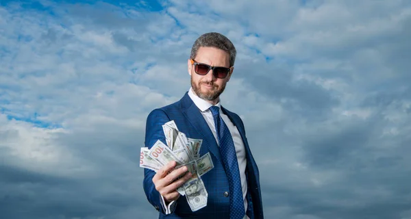 richness of man in glasses with money in suit. richness photo of man with money. richness of man with money on sky background. richness of man with money outdoor.