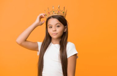 Zorlayıcı bir bebek. Çocuk prensesin altın taç sembolünü takıyor. Tatlı kız sarı arka planda dururken taç takıyor. Prenses konsepti ol. Prenses olmayı hayal eden her kız. Küçük hanım prenses..