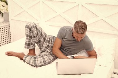 Evde dizüstü bilgisayarla serbest çalışan meşgul bir adamın fotoğrafı. Evde serbest çalışan bir adam var. Adam evde, yatakta serbest çalışıyor. Adam evde, yatak odasında serbest çalışıyor..