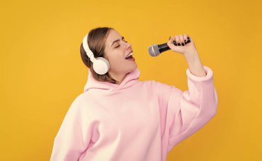 Sarı arka planda mikrofonu olan kulaklıklı genç bir kız..