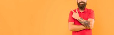 Happy bearded man crop view in casual red tshirt pointing finger aside yellow background copy space, advertise.