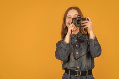 Mutlu çocuk fotoğrafçı sarı arkaplanı çekerken kameraya bakıyor, boşluğu kopyala.